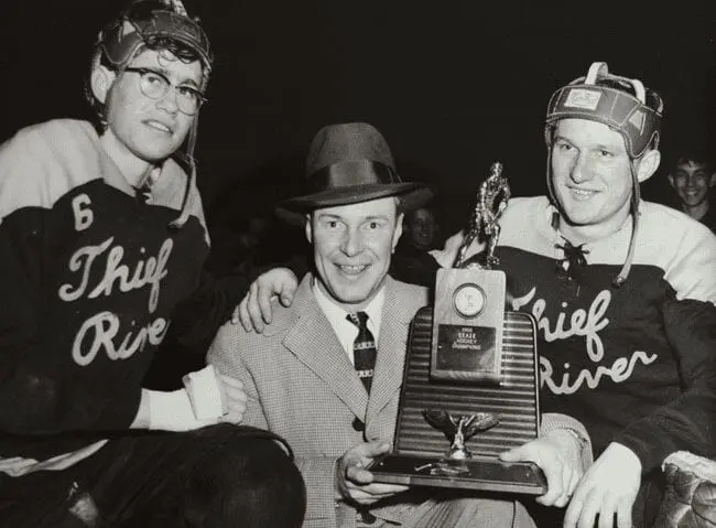 A man in a suit and hat holding a trophy.