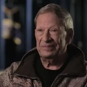 A man in a brown jacket is sitting down