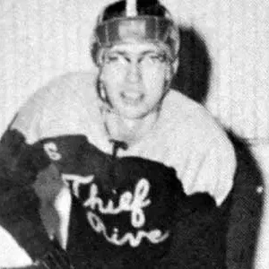 A man in a helmet and jersey is holding his hockey stick.