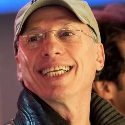 A man wearing glasses and a hat smiling.